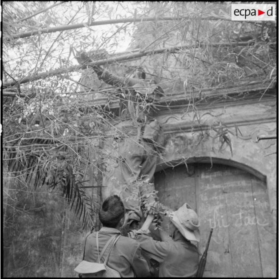 Des tirailleurs du bataillon de marche indochinois (BMI) escaladent  une des portes du village de Le Thon fermées à leur arrivée.