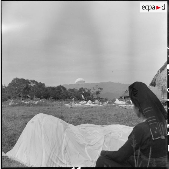 Une femme Thaï observe l'atterrissage des parachutes près des habitations dans la vallée de Diên biên Phu au cours de l'opération Castor.