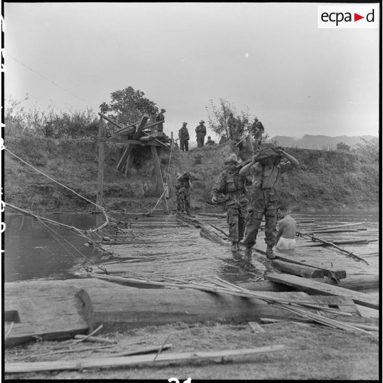 Des éléments du 35e régiment d'artillerie légère parachutiste (RALP) et des partisans franchissent la rivière Nam Youn chargés d’un canon de 75 mm sans recul largué par parachute.