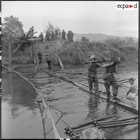 Des éléments du 35e régiment d'artillerie légère parachutiste (RALP) et des partisans franchissent la rivière Nam Youn chargés d’un canon de 75 mm sans recul largué par parachute.