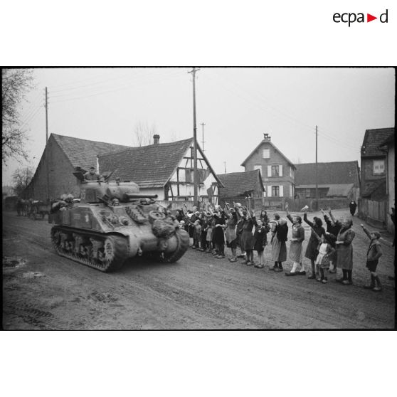 Le char Sherman de type M4A2 "Corse", du 2e escadron du 12e RCA (régiment de chasseurs d'Afrique) appartenant au GTL, le Groupement tactique de Langlade, traverse un village alsacien, probablement près d'Obernai (Bas-Rhin), acclamé par les habitants.