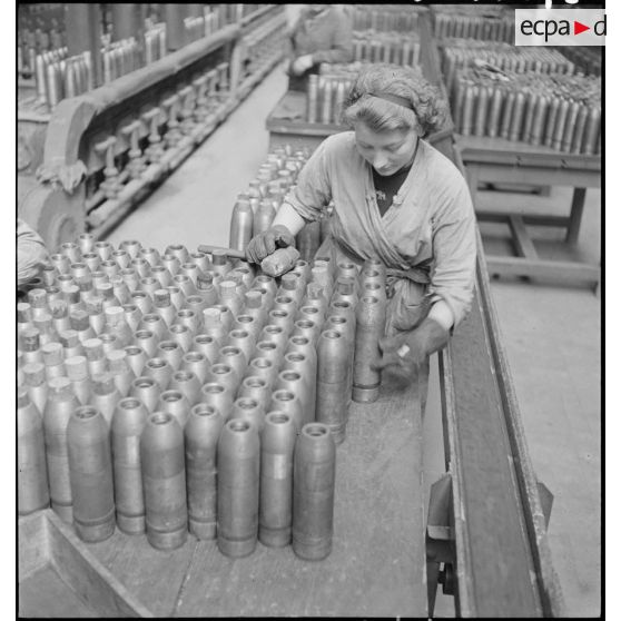 Dans une cartoucherie ou un atelier de fabrication, des ouvrières ferment des enveloppes d'obus de 75 mm avec des bouchons de bois.