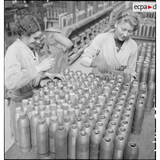 Dans une cartoucherie ou un atelier de fabrication, des ouvrières ferment des enveloppes d'obus de 75 mm avec des bouchons de bois.