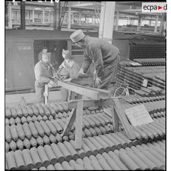 Dans une cartoucherie ou un atelier de fabrication, des ouvriers et des soldats chargent des obus de 75 mm, modèle 1917, dans un wagon de chemin de fer.