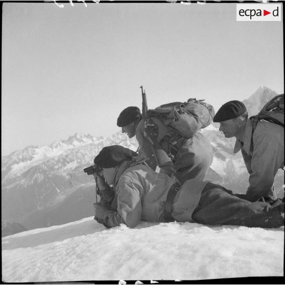 Trois éclaireurs du 199e BCHM allongés ou à genoux dans la neige observent aux jumelles.