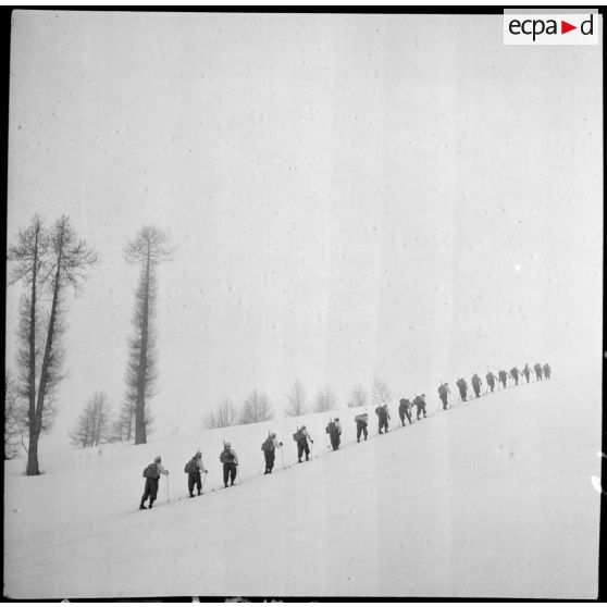 Une section d'éclaireurs-skieurs en mission de reconnaissance gravit une pente enneigée.