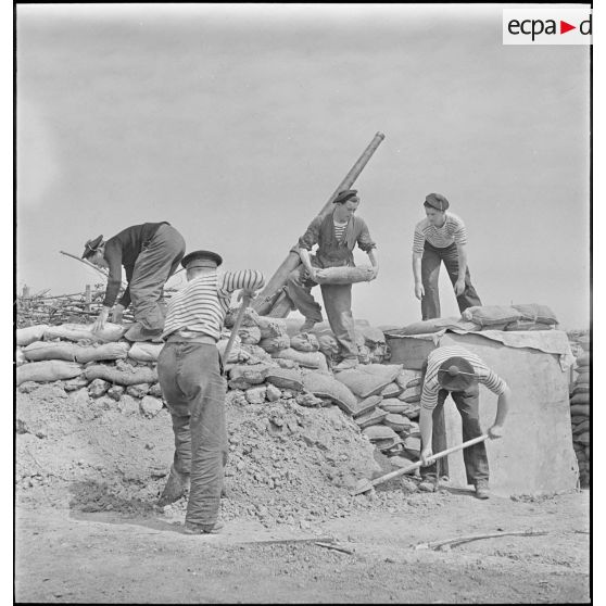 Des marins, appartenant à la 4e batterie mobile de défense antiaérienne de la Marine, effectuent des travaux de terrassement et empilent des sacs de sable afin de consolider la protection autour d'un canon antiaérien de 90 mm.