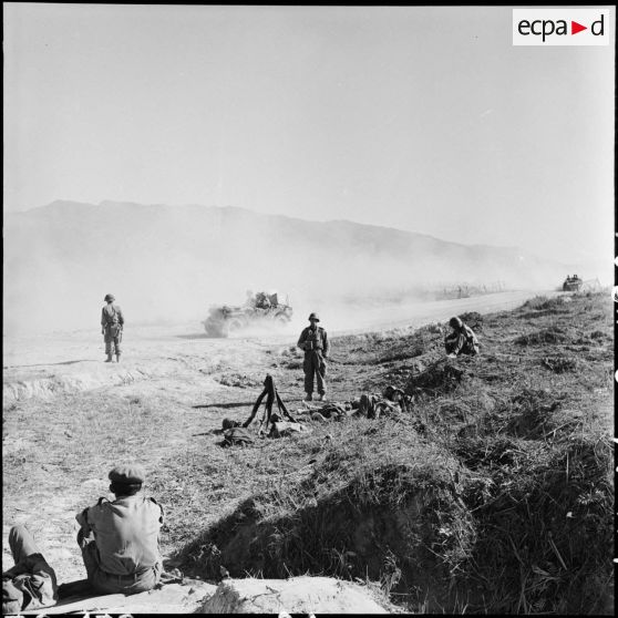 Circulation sur la route qui traverse le camp de Diên Biên Phu tandis que des soldats sont au repos sur le bas-côté.