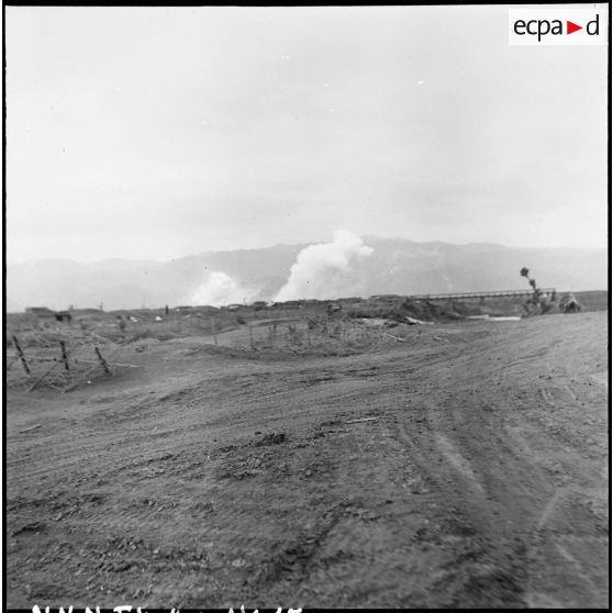 De la fumée s'élève en direction du poste de commandement du centre du camp retranché de Diên Biên Phu, non loin du pont Bailey qui enjambe la rivière Nam Youn.