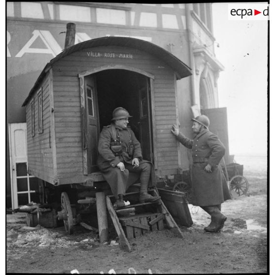 Deux soldats se tiennent à l'entrée d'une roulotte qui les abrite.