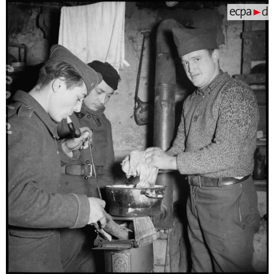 Photographie de groupe de soldats réunis autour d'un poêle à l'intérieur d'un baraquement.