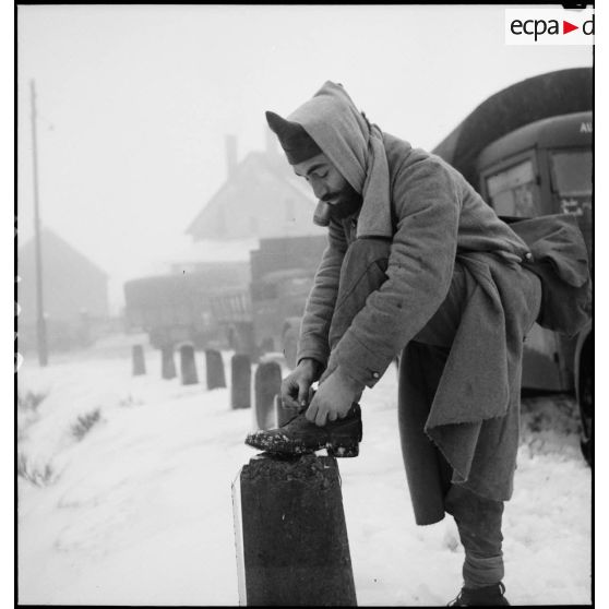 Un soldat de la 2e armée fait ses lacets dasn un paysage enneigé.