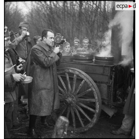 Un caméraman du SCA filme alors que des soldats de la 2e armée mangent debout près d'une cuisine roulante.