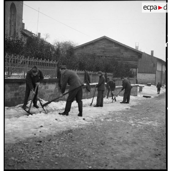 Plan général de soldats qui déblayent de la neige accumulée sur un trottoir.