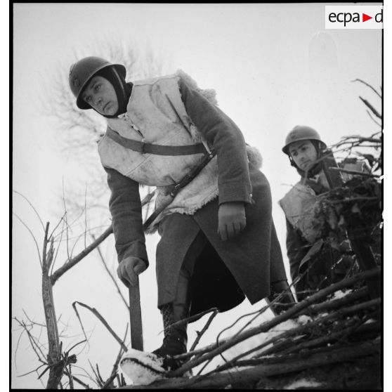 Près de la frontière belge un soldat est photographié en plan moyen en contre-plongée alors qu'il part en patrouille dans la neige.