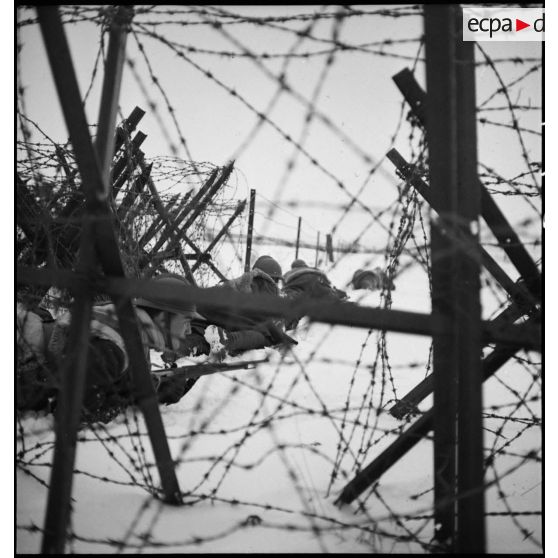 Plan moyen de soldats en patrouille qui rampent dans la neige le long d'un réseau de barbelés.