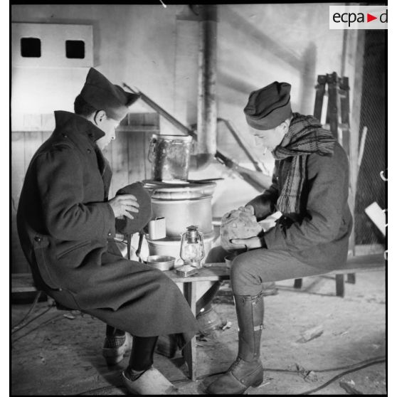 Dans une pièce, photographie de groupe de soldats qui mangent près d'un poêle.