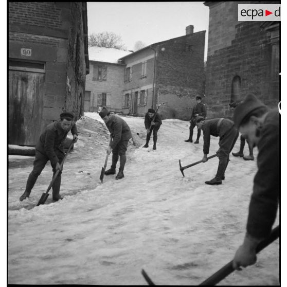 Plan général de soldats qui déblayent de la neige accumulée dans la rue d'un village.