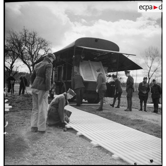 Des soldats déchargent les caillebotis de bois du camion-douche de la SHLD (section d'hygiène, lavage et désinfection) de la 2e armée.