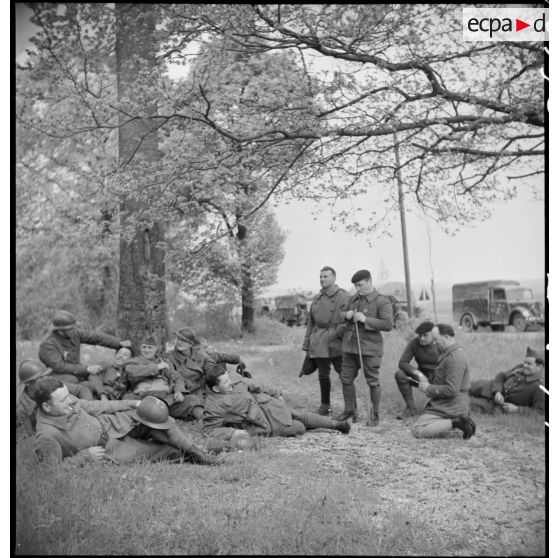 Des soldats et des conducteurs d'une colonne motorisée française se reposent en bordure d'une route.