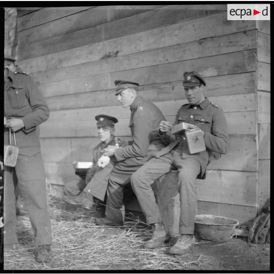 Des soldats anglais de la BEF mangent assis près d'un baraquement.