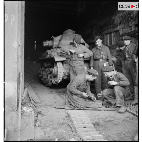 Des mécaniciens réparent le train de roulement d'un char R35 du 5e BCC dans une grange.