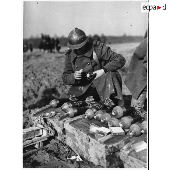 Un soldat de la 4e armée manipule des obus de mortier de 81 mm qui sont rangés au sol devant lui.