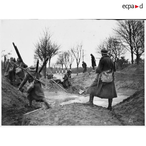 Des soldats de la 4e armée, qui portent des madriers, contournent un trou d'obus sur une route de Lorraine.