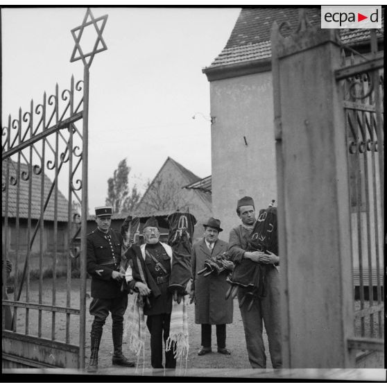 Devant une synagogue un aumônier militaire de confession juive évacue les tables de la Loi aidé de gendarmes.