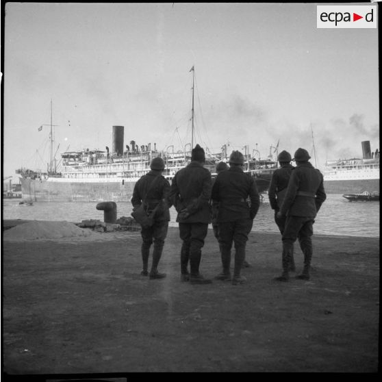 Sur le port de Marseille des soldats de la 6e armée, photographiés de dos, regardent un cargo à quai.