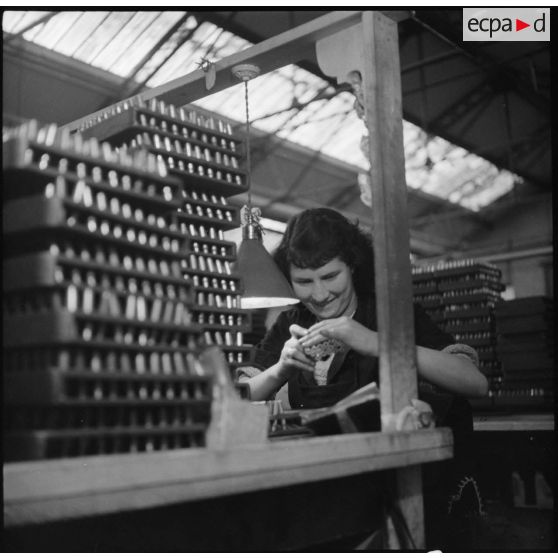 Dans l'usine, portrait d'une ouvrière qui vérifie la taille et le calibre des cartouches en fin de chaîne.