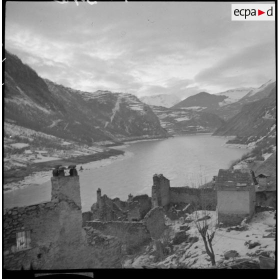 Un lac de montagne est photographié en plan général avec le massif montagneux enneigé en arrière plan.