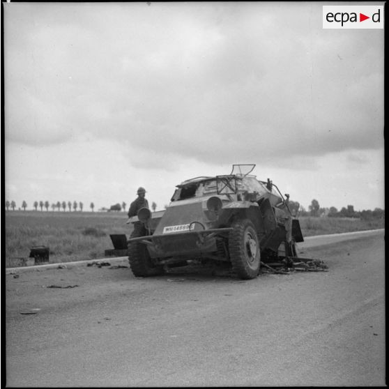 Un soldat français observe un véhicule allemand abandonné au bord d'une route.