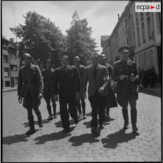 Des soldats français, un officier britannique et des civils marchent dans une rue.