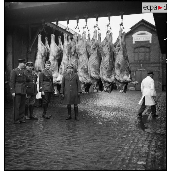 Officiers devant des carcasses de viande accroché dans la cour d'un abattoir.