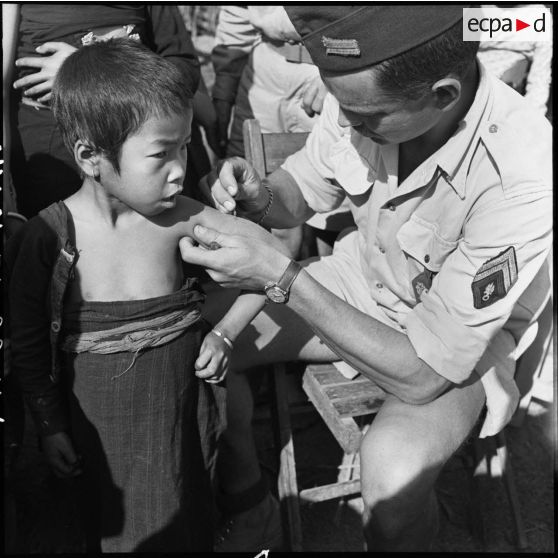 Vaccination d'un enfant Thaï par un sergent légionnaire dans un village de la vallée de Diên Biên Phu.