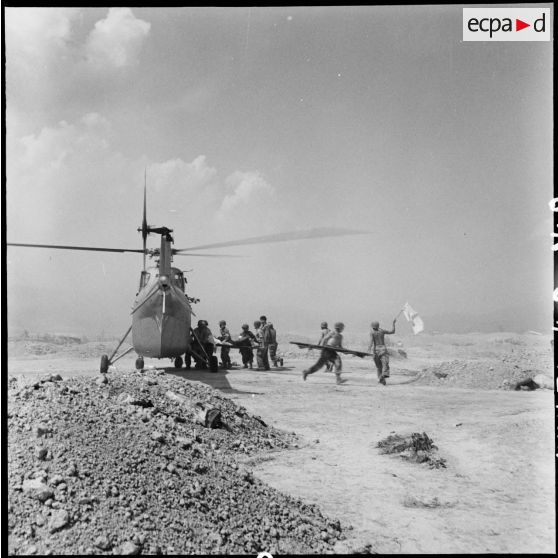 Embarquement de blessés dans un hélicoptère Sikorksy S55 au cours d'une évacuation sanitaire à Diên Biên Phu, sous le feu de l'artillerie Viêt-minh malgré les fanions à croix rouge agités par les brancardiers.