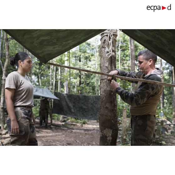 Une stagiaire du régiment du service militaire adapté (RSMA) tend une bâche supervisé par un instructeur pour le montage d'un bivouac lors d'un atelier jungle à Saint-Jean-du-Maroni, en Guyane française.