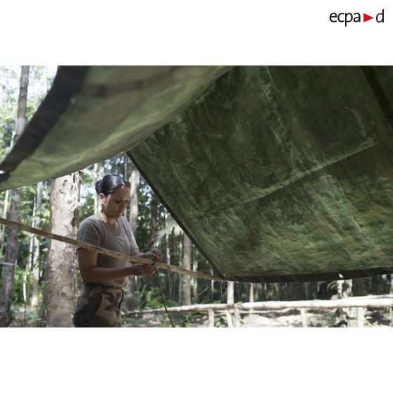 Une stagiaire du régiment du service militaire adapté (RSMA) tend une bâche pour le montage d'un bivouac lors d'un atelier jungle à Saint-Jean-du-Maroni, en Guyane française.