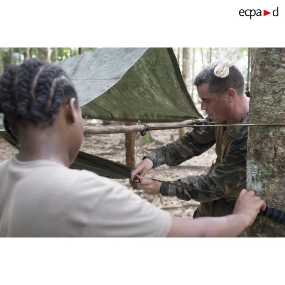 Un instructeur supervise l'installation d'un hamac par une stagiaire du régiment du service militaire adapté (RSMA) pour le montage d'un bivouac lors d'un atelier jungle à Saint-Jean-du-Maroni, en Guyane française.