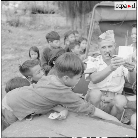 Distribution de documents aux enfants de la communauté catholique de Yen Vi par des militaires se déplaçant à bord d'une jeep.