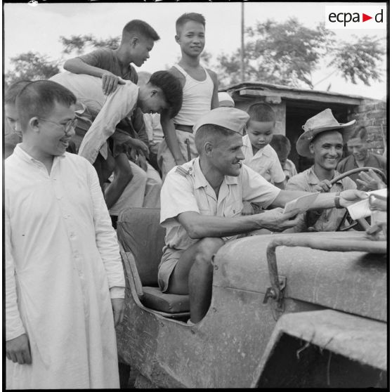 Distribution de documents aux enfants de la communauté catholique de Yen Vi par des militaires se déplaçant à bord d'une jeep.