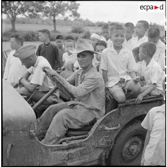 Distribution de documents aux enfants de la communauté catholique de Yen Vi par des militaires se déplaçant à bord d'une jeep.