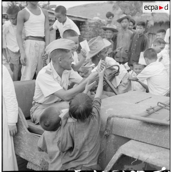 Distribution de documents aux enfants de la communauté catholique de Yen Vi par des militaires se déplaçant à bord d'une jeep.