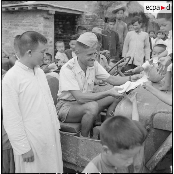 Distribution de documents aux enfants de la communauté catholique de Yen Vi par des militaires se déplaçant à bord d'une jeep.