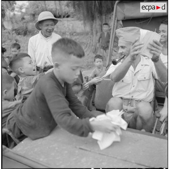 Distribution de documents aux enfants de la communauté catholique de Yen Vi par des militaires se déplaçant à bord d'une jeep.