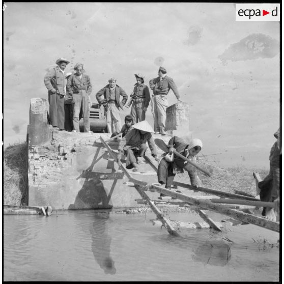 Passage de travailleurs vietnamiens sur des planches de bois remplaçant un pont détruit sur la route coloniale n°1 au Tonkin. A l'arrière-plan, des éléments du Génie.