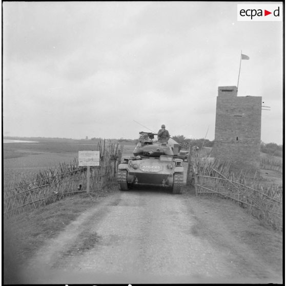 Progression d'une colonne de blindés du 1er régiment de chasseurs à cheval sur une route au Tonkin. En tête, un char M24 Chaffee passe près d'une tour de guet fortifiée.