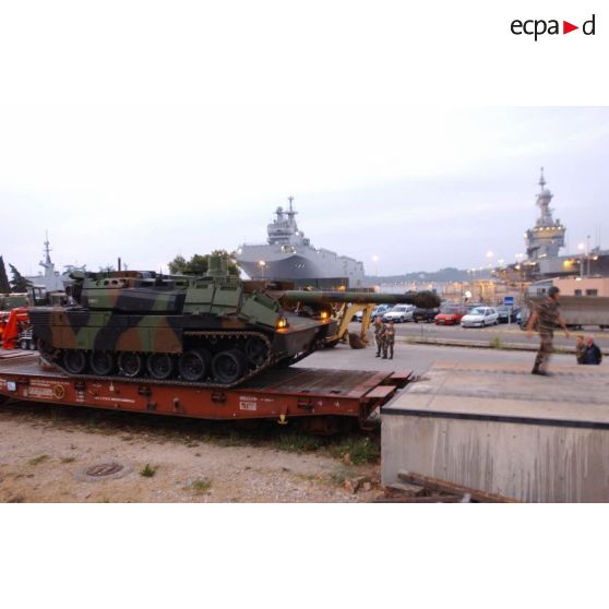 Sortie des wagons du char Leclerc Evreux du 6/12e RC (régiment de cuirassiers) à la gare de ferroutage de l'arsenal de Toulon. En arrière-plan, le BPC (bâtiment de projection et de commandement) Mistral et le porte-avions nucléaire Charles-de-Gaulle à quai.