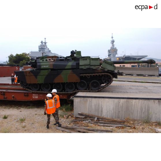 Sortie des wagons du char Leclerc Le Vigilant du 6/12e RC (régiment de cuirassiers) à la gare de ferroutage de l'arsenal de Toulon. En arrière-plan, le BPC (bâtiment de projection et de commandement) Mistral et le porte-avions nucléaire Charles-de-Gaulle à quai.